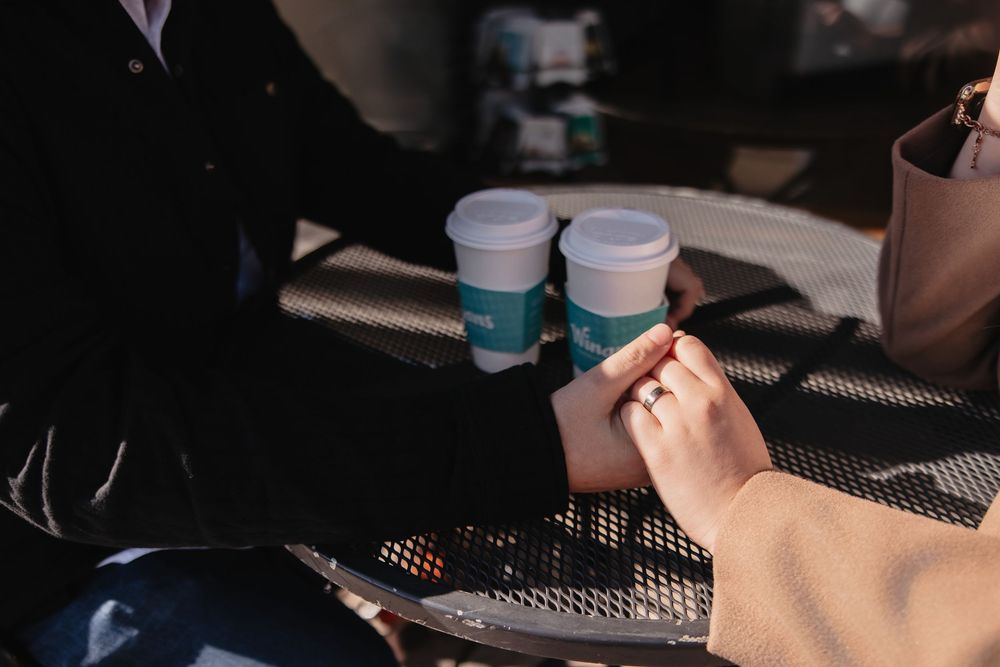 Two coffee cups and hands on a metal patio table in moody lighting.