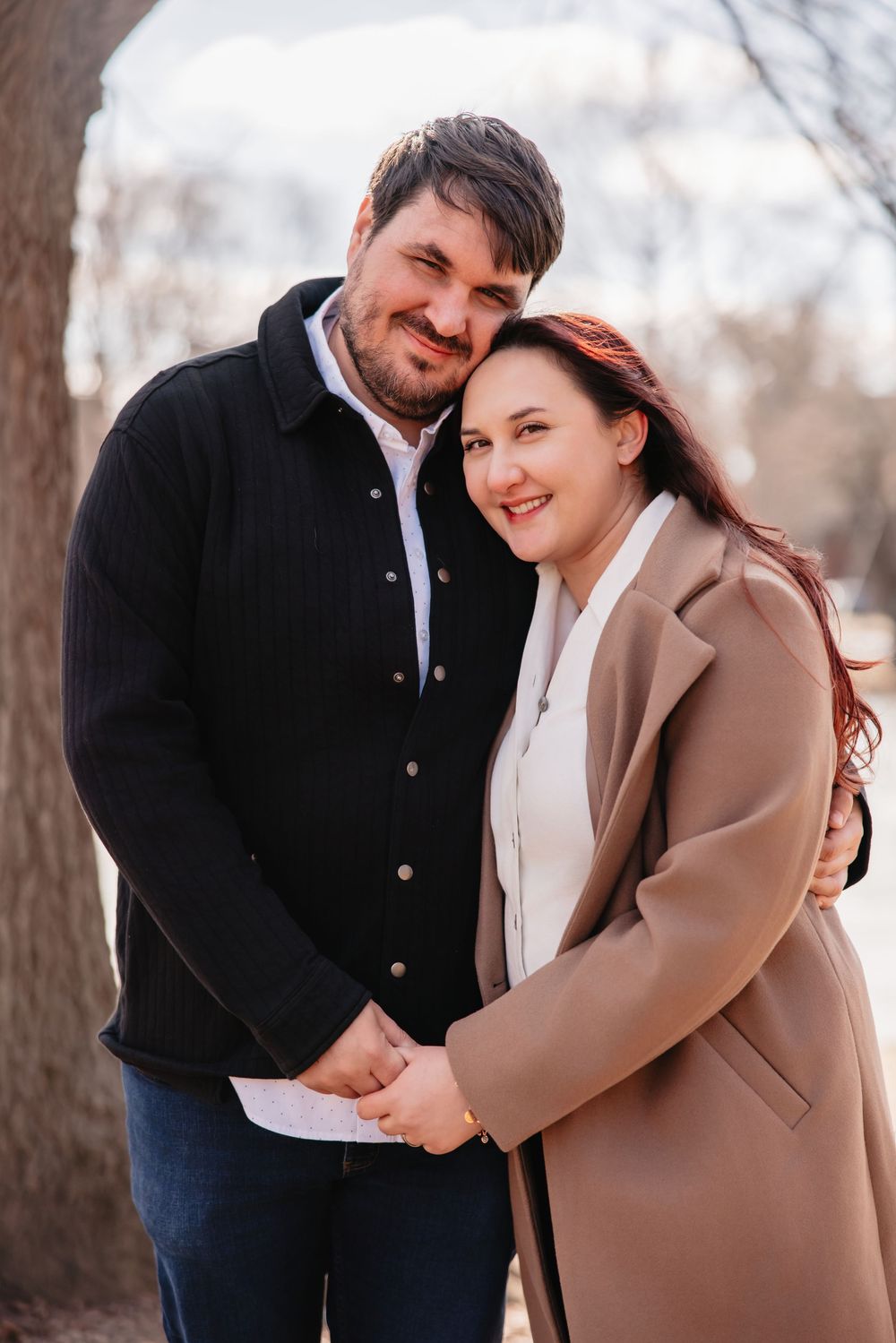 A couple in winter coats shares a tender moment outdoors on a cold autumn day.