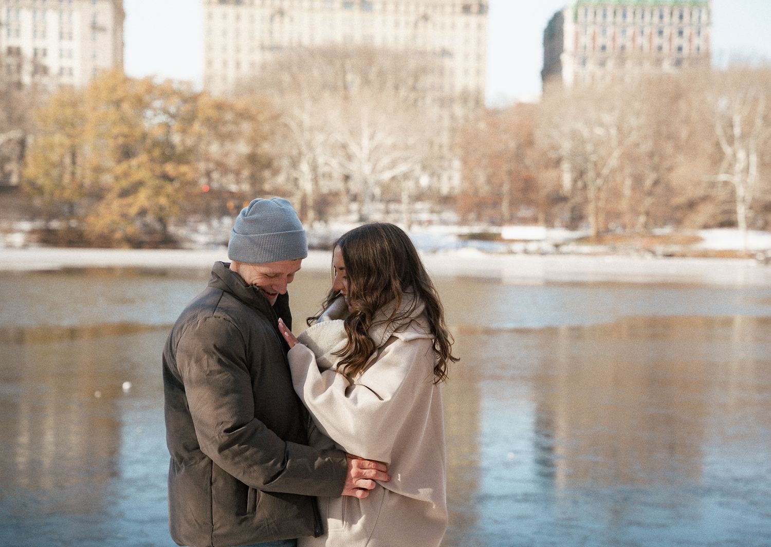 A romantic winter scene by a lake with New York City buildings in the background.
