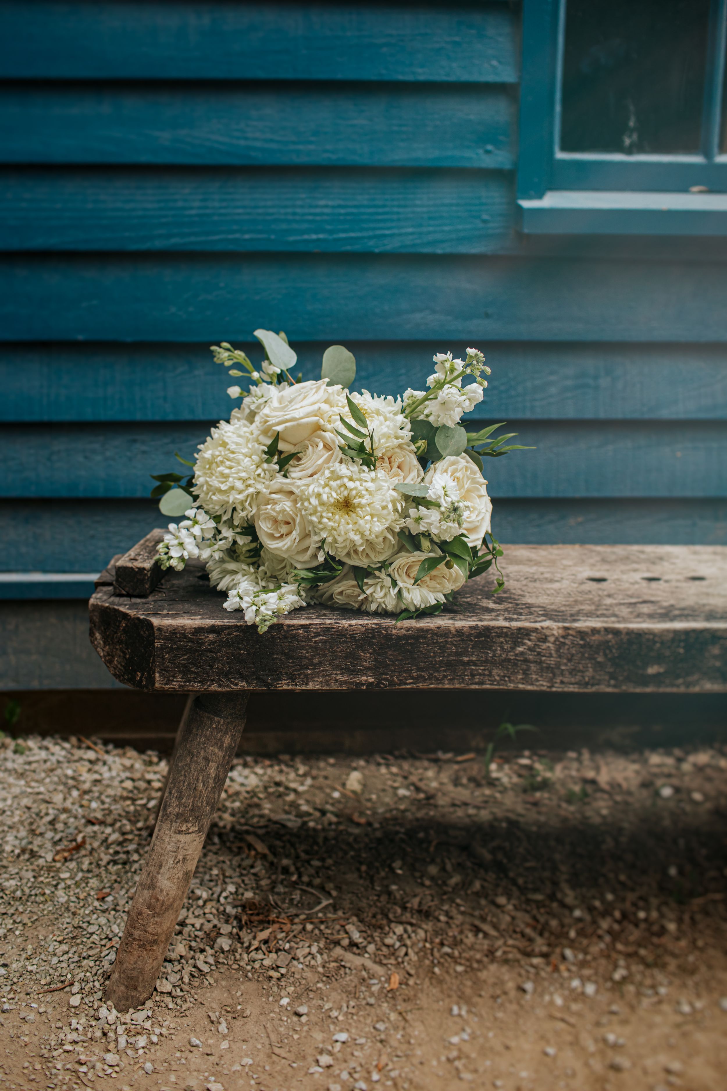 White wedding bouquet resting on rustic wooden bench against blue wall.