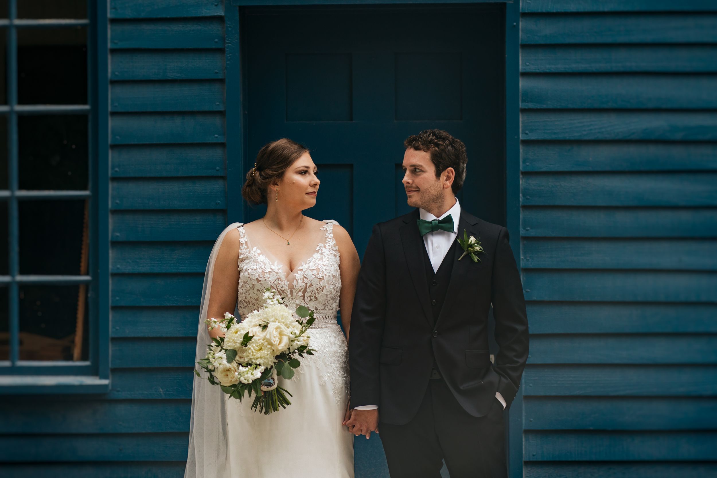 A bride and groom share a romantic moment in front of a blue wooden wall during their wedding photoshoot. Conner Prairie, Fishers Indiana