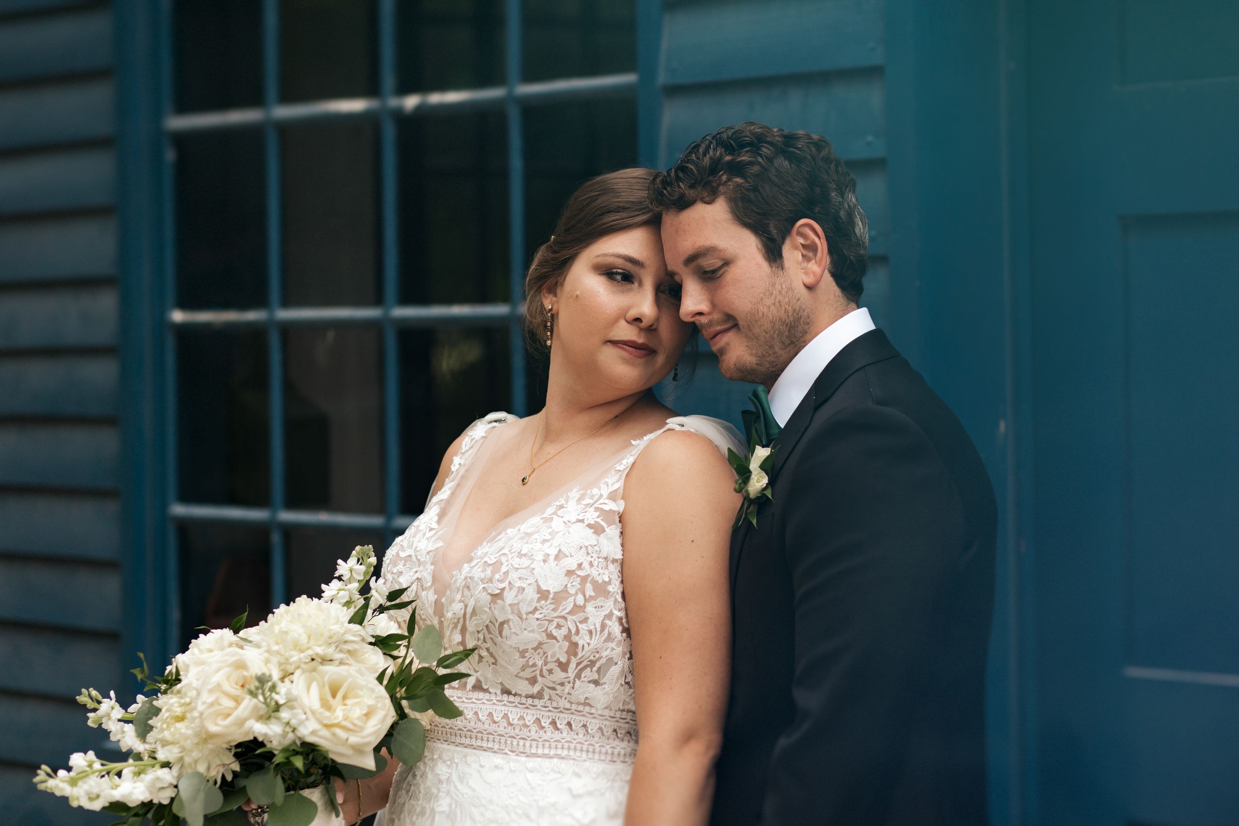 A romantic wedding portrait against a teal blue wall with white floral bouquet.