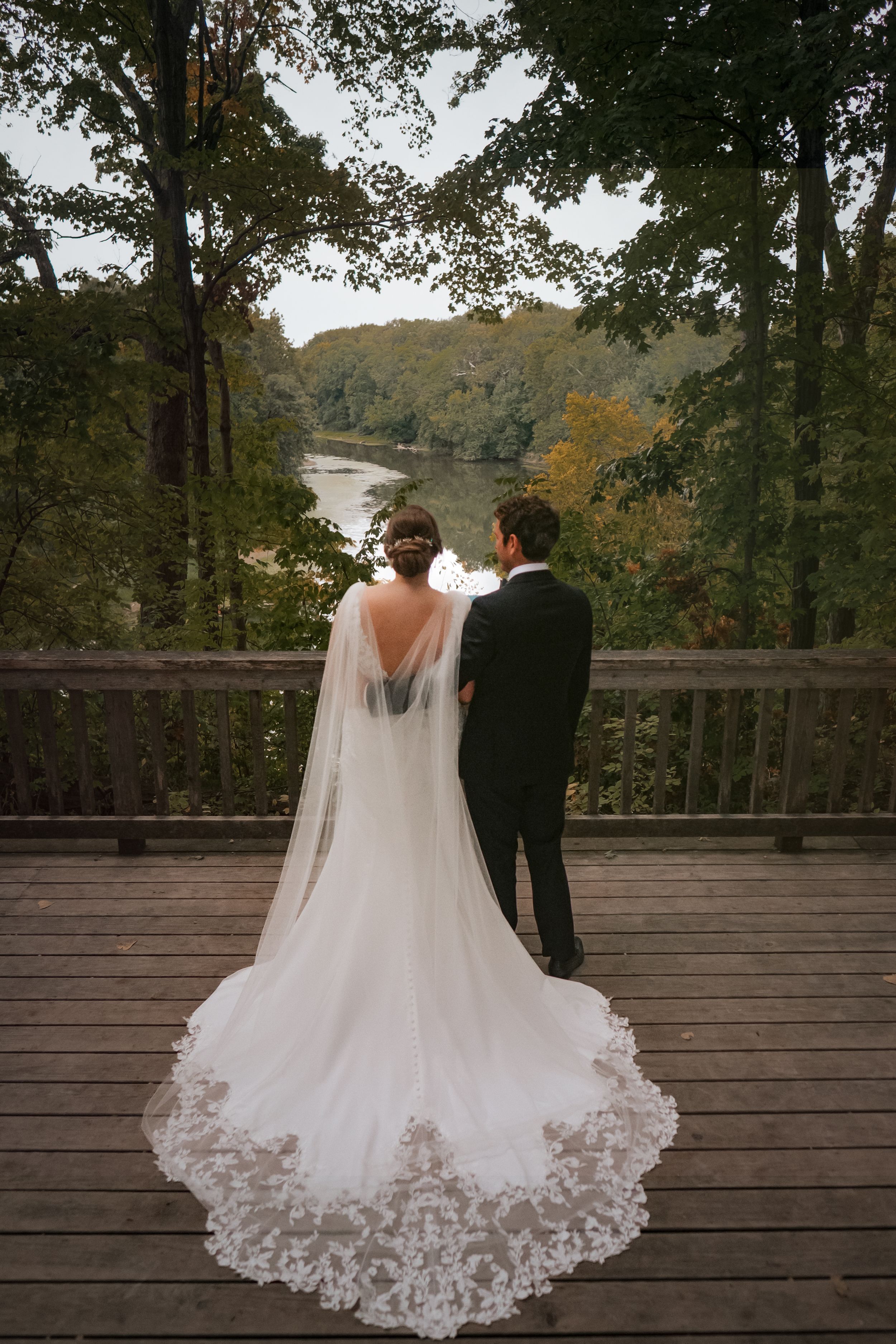 A scenic wedding photo overlooking an autumn river from a wooden observation deck.