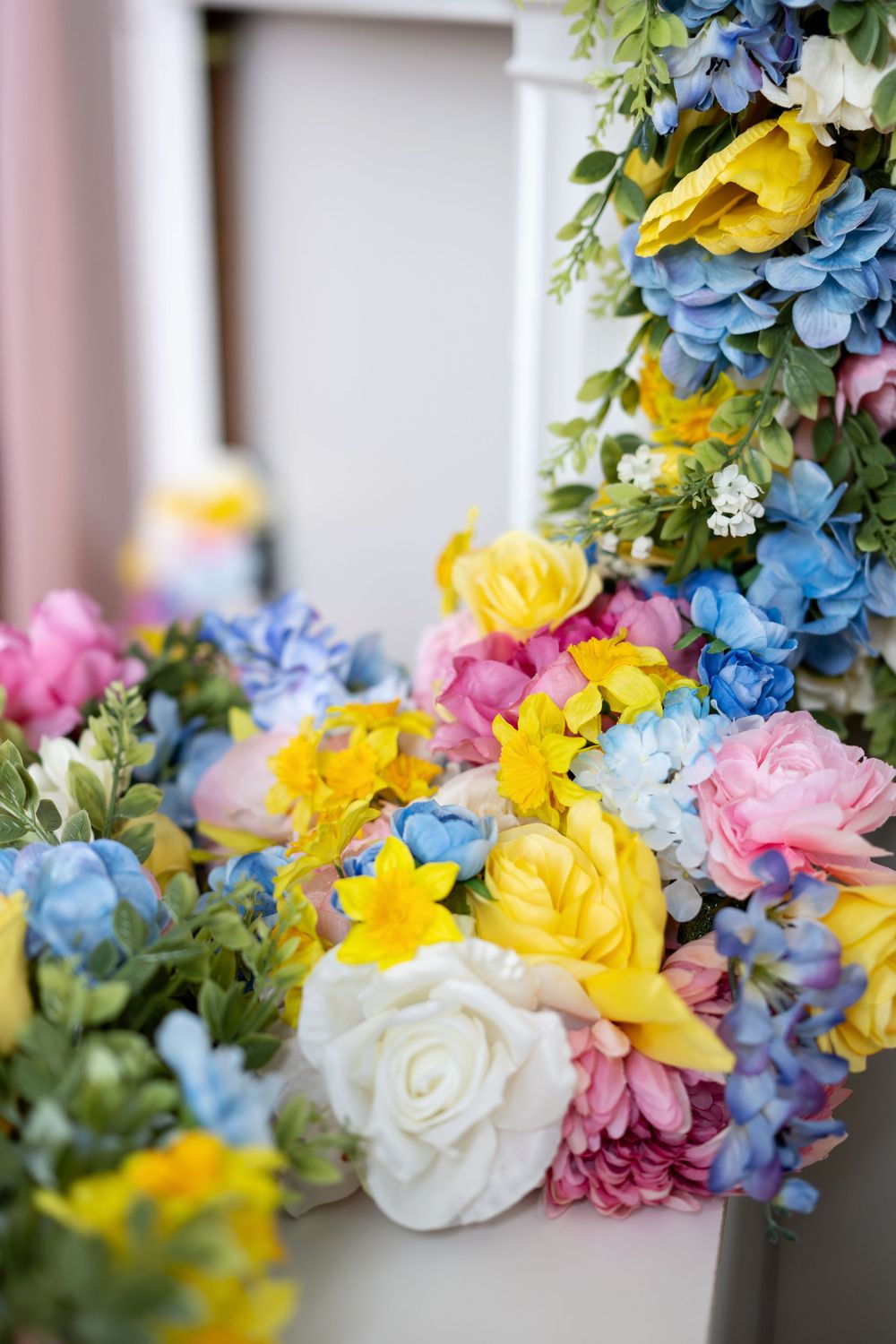 Vibrant bouquet of yellow, pink, blue, and white artificial flowers arranged in a decorative white container.