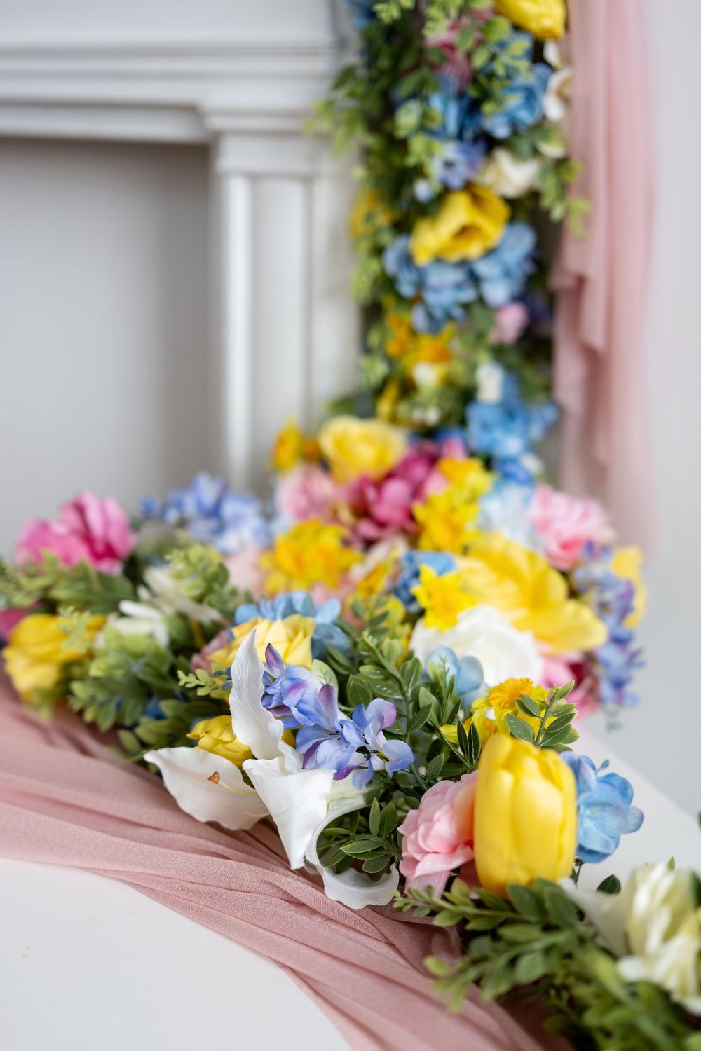 Colorful spring flower arrangements with yellow, pink, blue, and white blooms displayed on a pink fabric-covered surface.