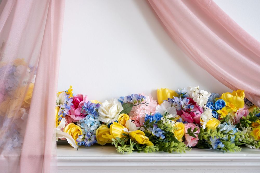 Colorful spring floral garland with pink, yellow, and blue flowers on a white mantel with pink draping.