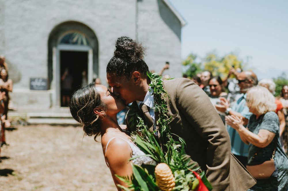 Wedding guests celebrate joyfully during an outdoor ceremony with tropical greenery and leis.