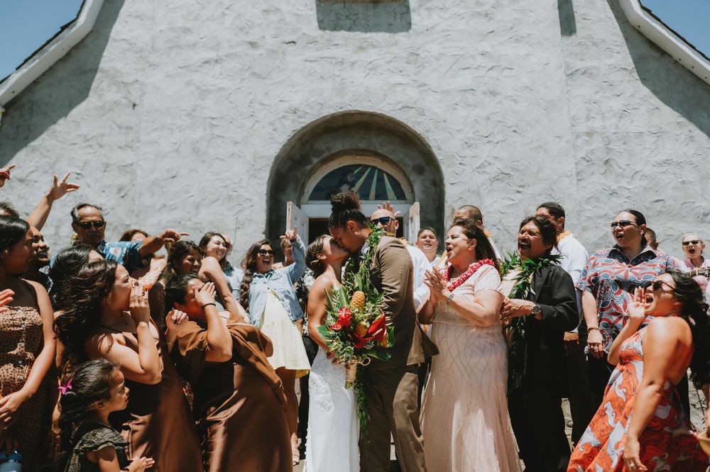 Guests gathered at a sunny outdoor wedding ceremony with white church building in background.
