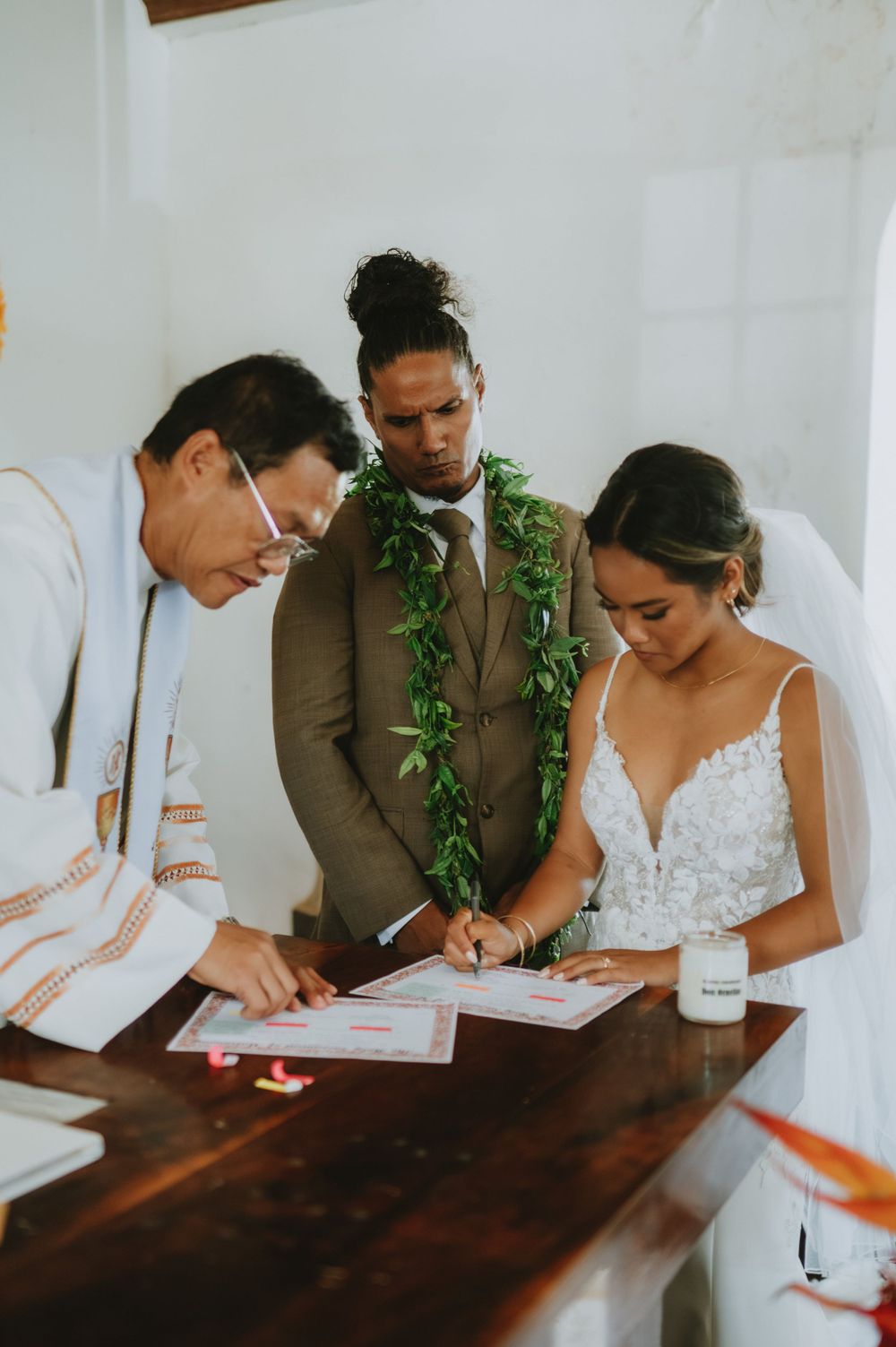 Newlyweds signing official documents at wooden table during intimate church ceremony.