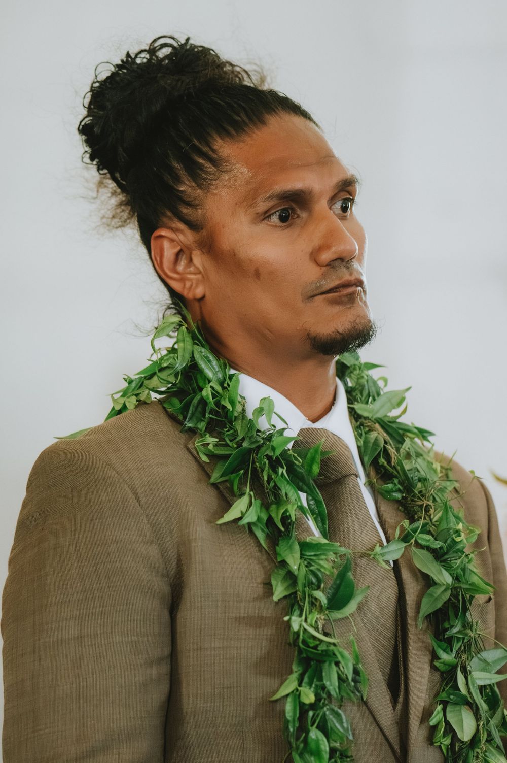 Wedding party member wearing a traditional Hawaiian maile lei and tan suit poses for portraits.