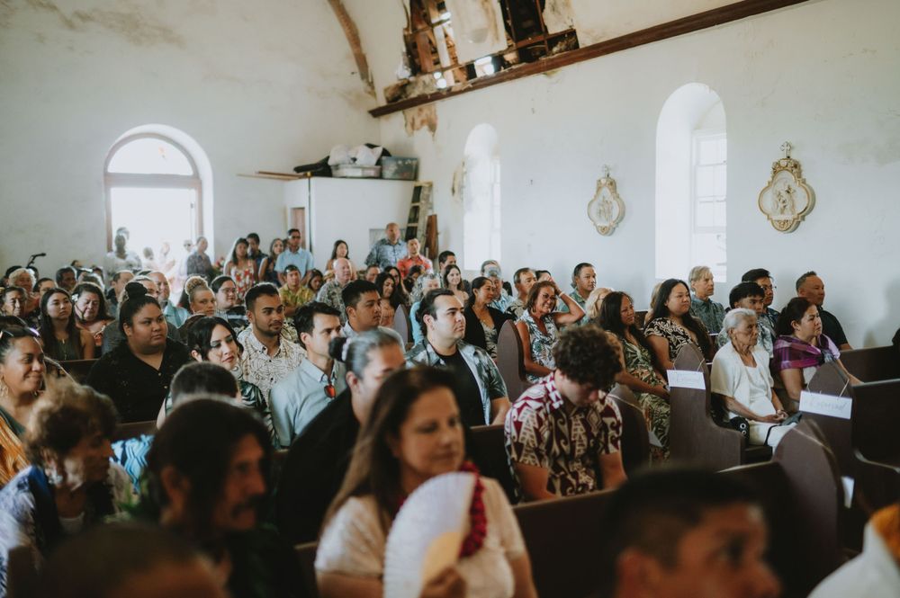 Wedding ceremony attendees fill the pews of a traditional white church interior.
