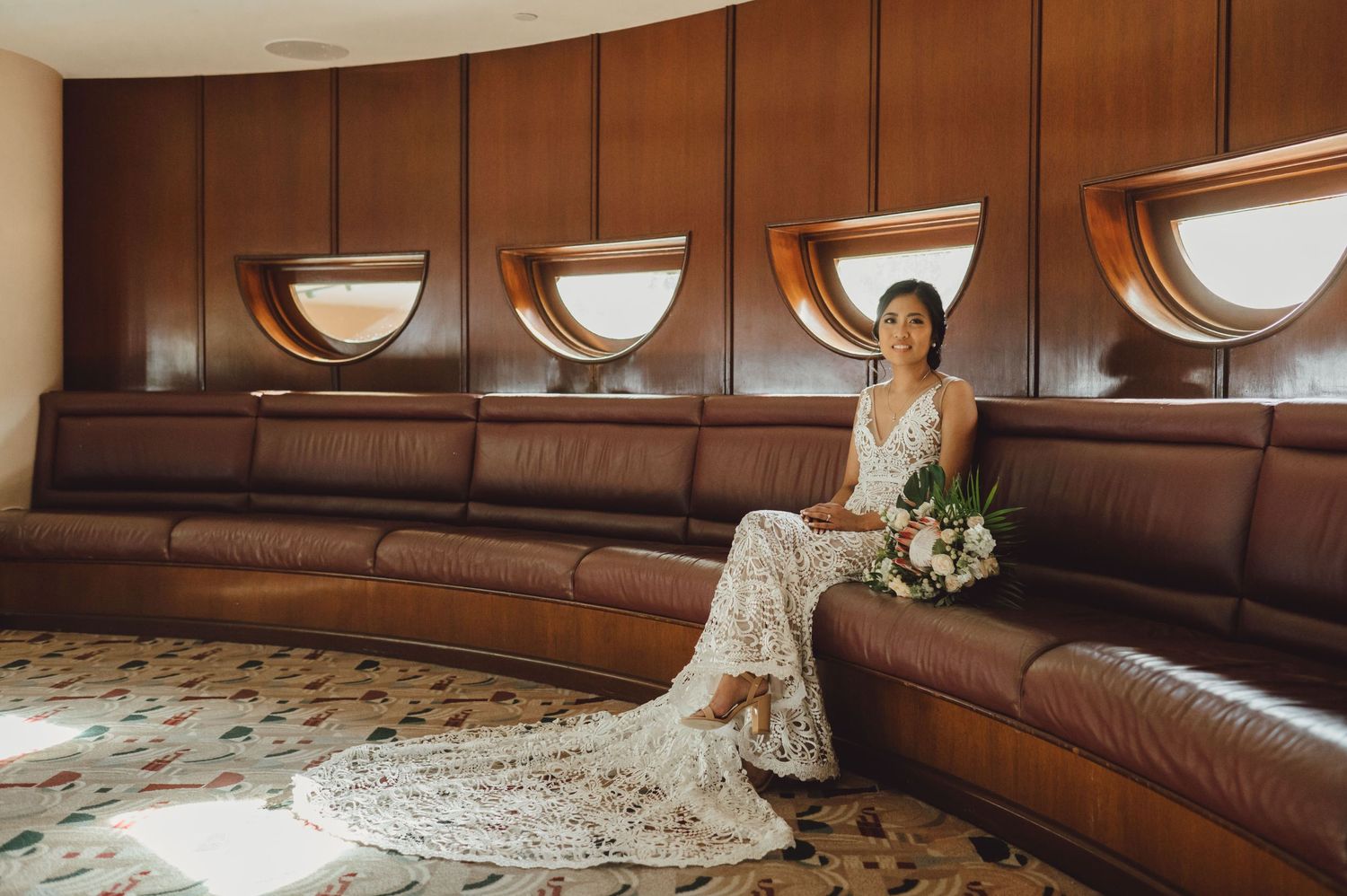 Elegant bridal portrait on curved brown leather seating with modern architectural details.