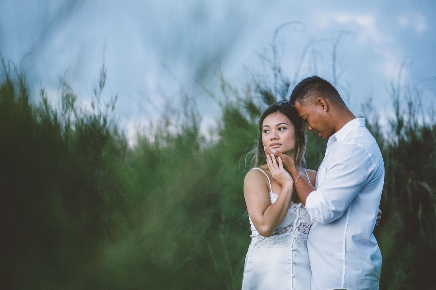 Romantic couple embraces outdoors during golden hour photoshoot in white attire.