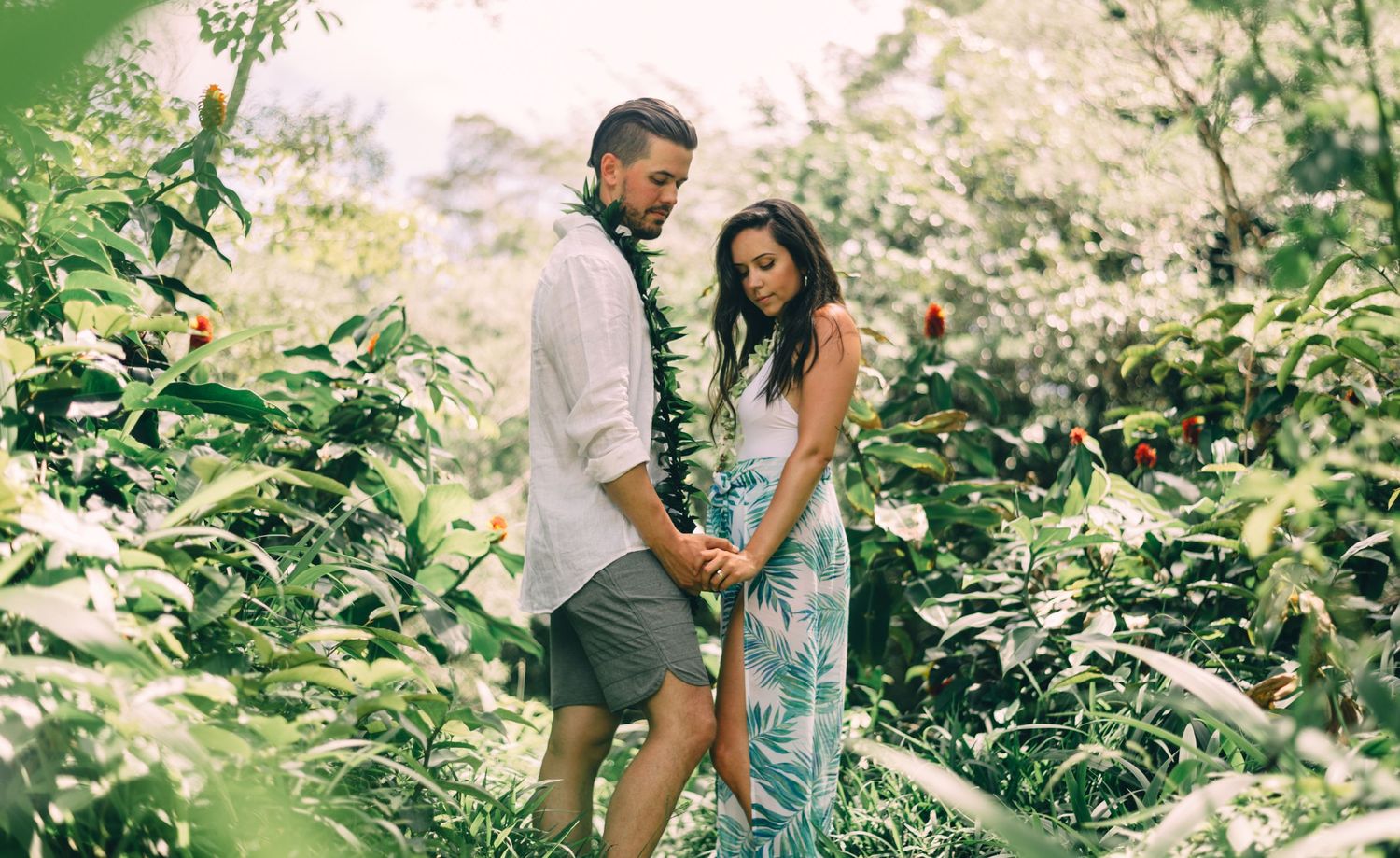 A romantic couple explores a lush tropical garden path together wearing coordinated outfits.