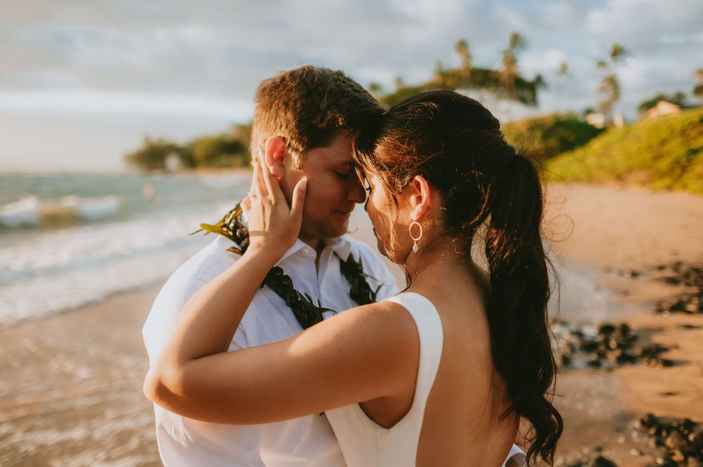 Couple embracing on a scenic beach with waves and palm trees in the background.