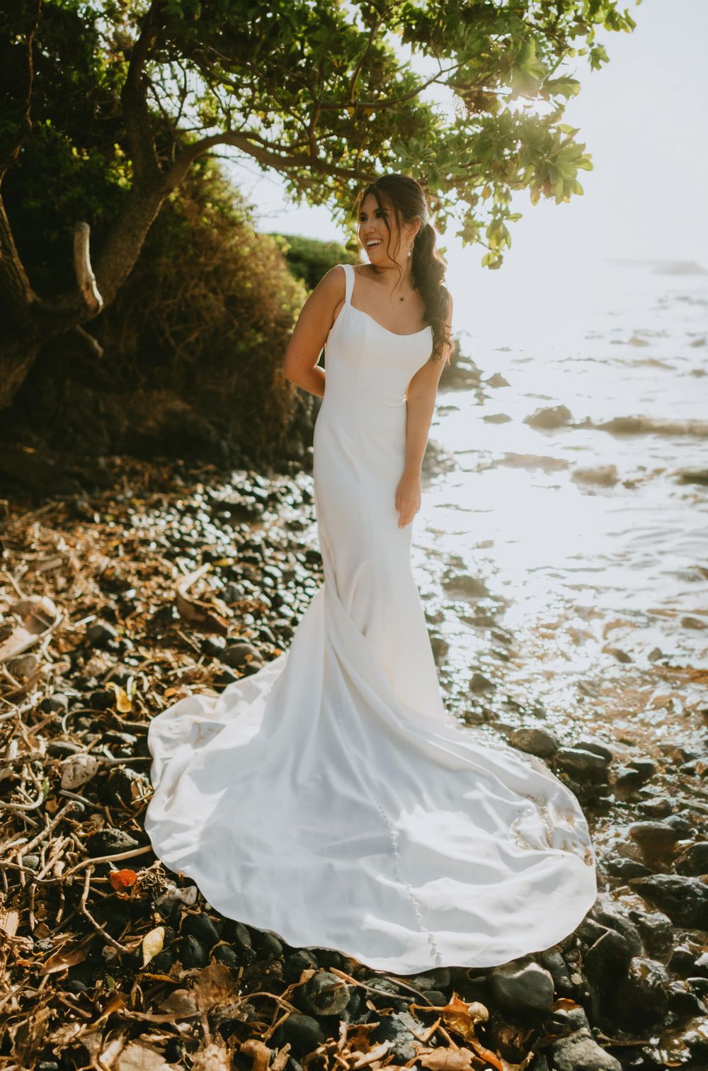 White wedding dress flowing gracefully against rocky beach landscape at sunset.
