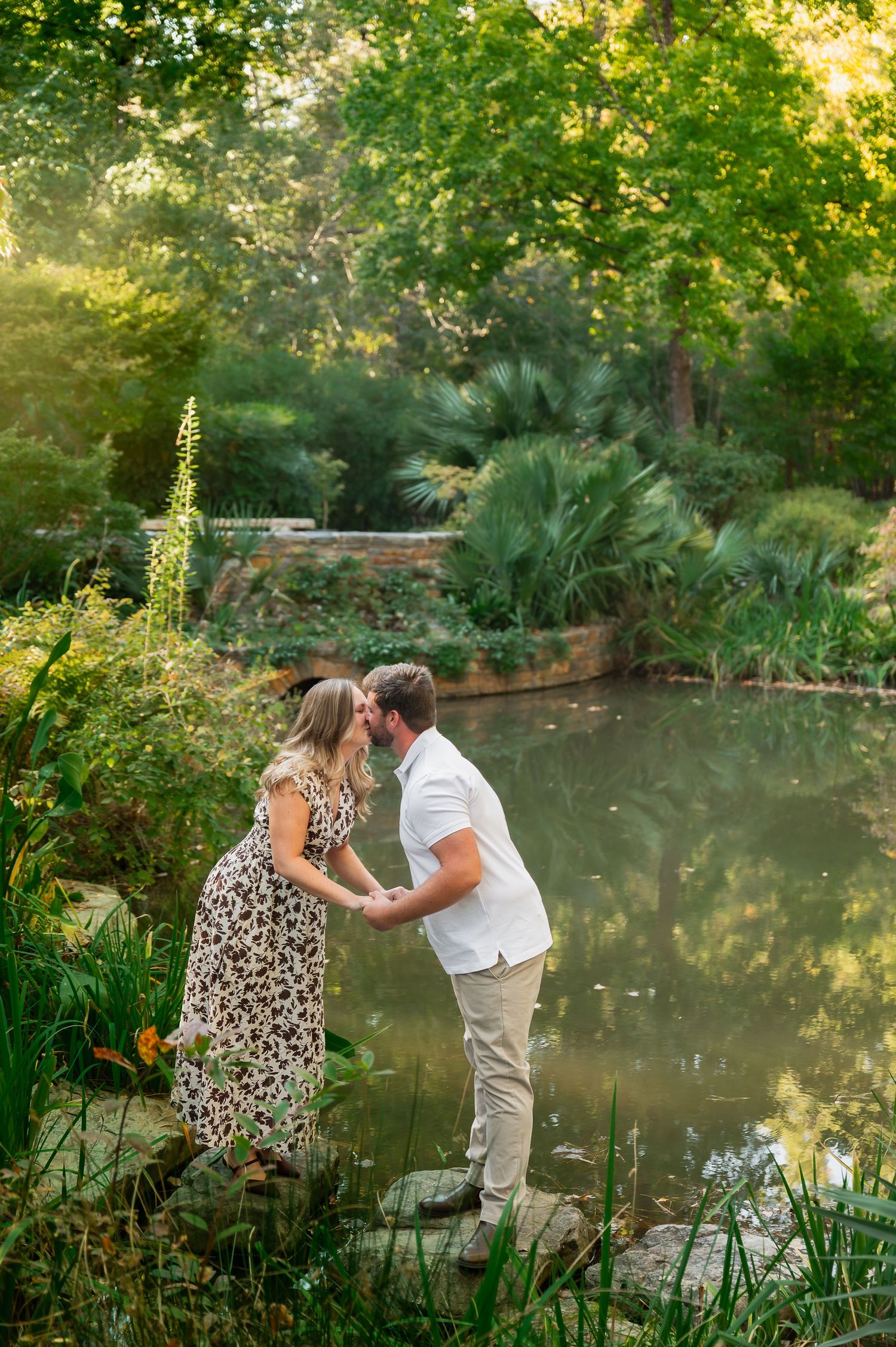 Romantic couple sharing tender moments by a tranquil garden pond at golden hour.