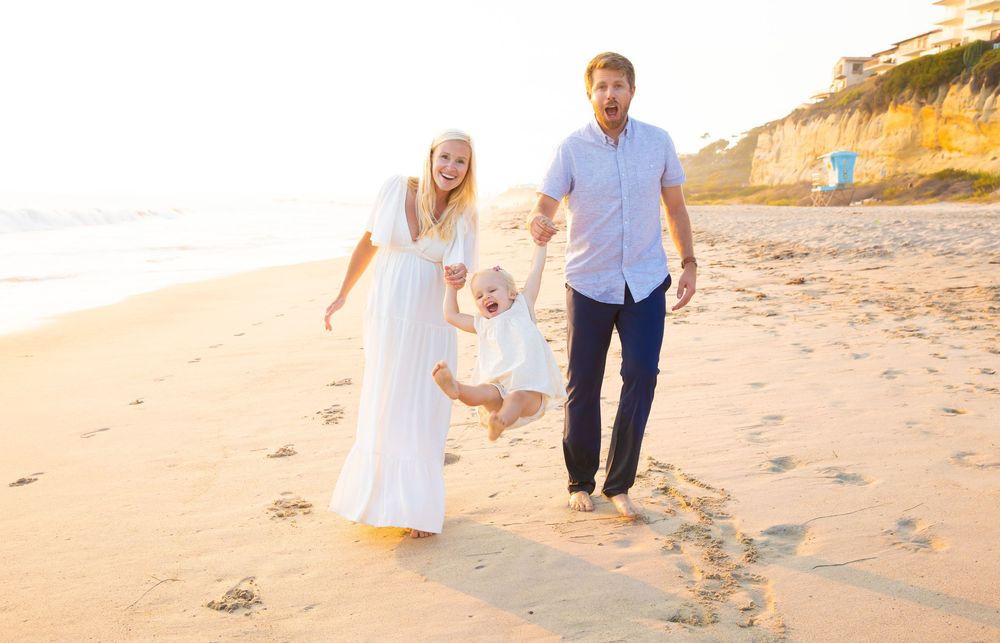 A family walks together along a sandy beach at sunset with cliffs in the background.