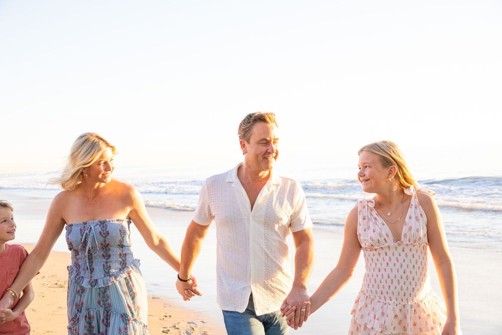 A happy family walks together along a sunny beach at sunset, holding hands and smiling.