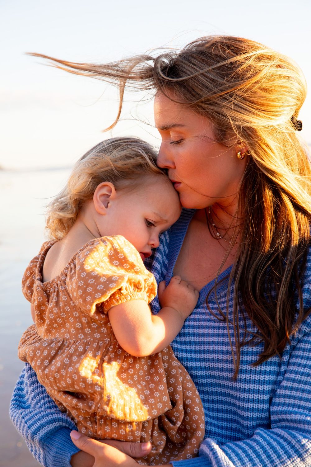 A tender embrace between parent and child backlit by golden sunlight, wearing blue and floral patterns.