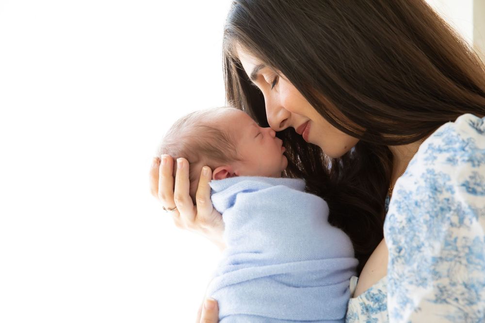 A tender moment between parent and newborn baby wrapped in soft blue blanket against bright background.