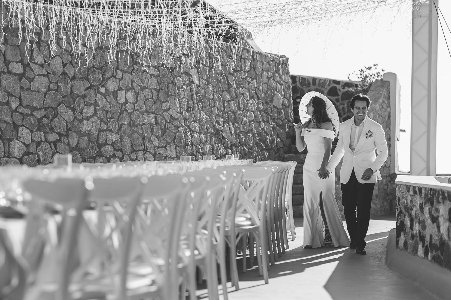 A black and white photo sequence shows a Santorini couple walking together alongside a banqueting table at their destination wedding.