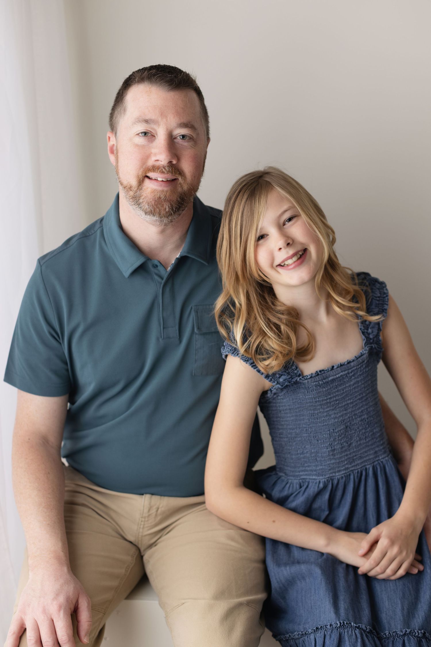 A parent and child pose together for a portrait, wearing a blue polo shirt and navy dress against a light background. Elizabeth Lang Photogr