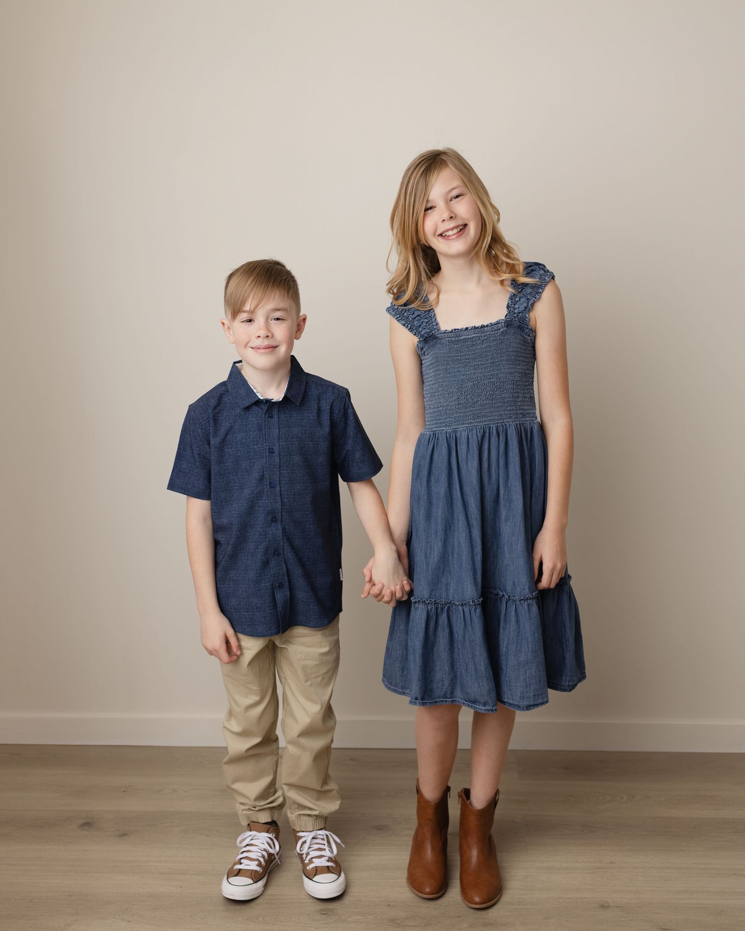 Two children in coordinating navy blue and denim outfits stand together on a light-colored floor. Elizabeth Lang Photography Surrey