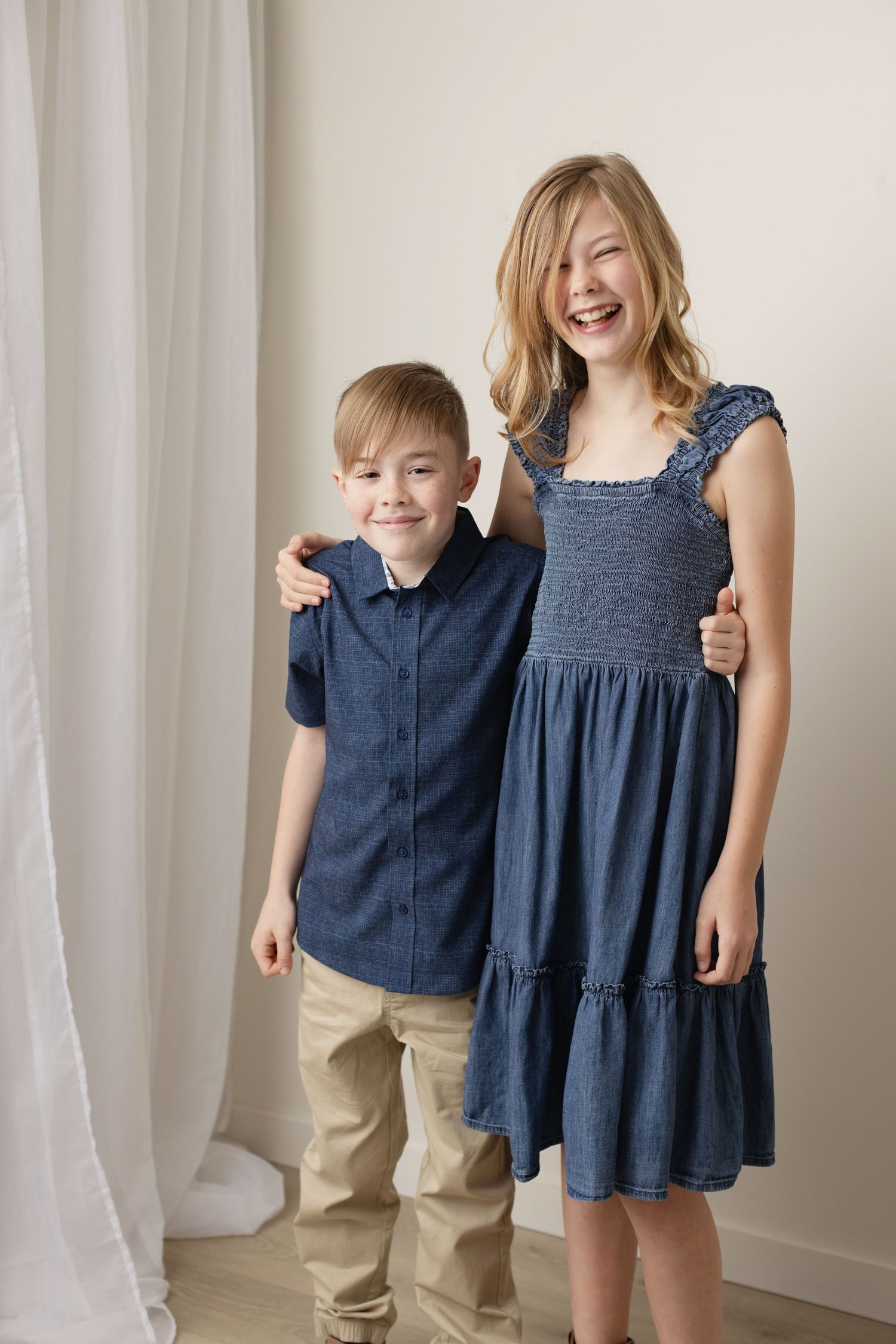 Two people wearing coordinating navy blue outfits pose together against a light curtain background. Elizabeth Lang Photography Surrey