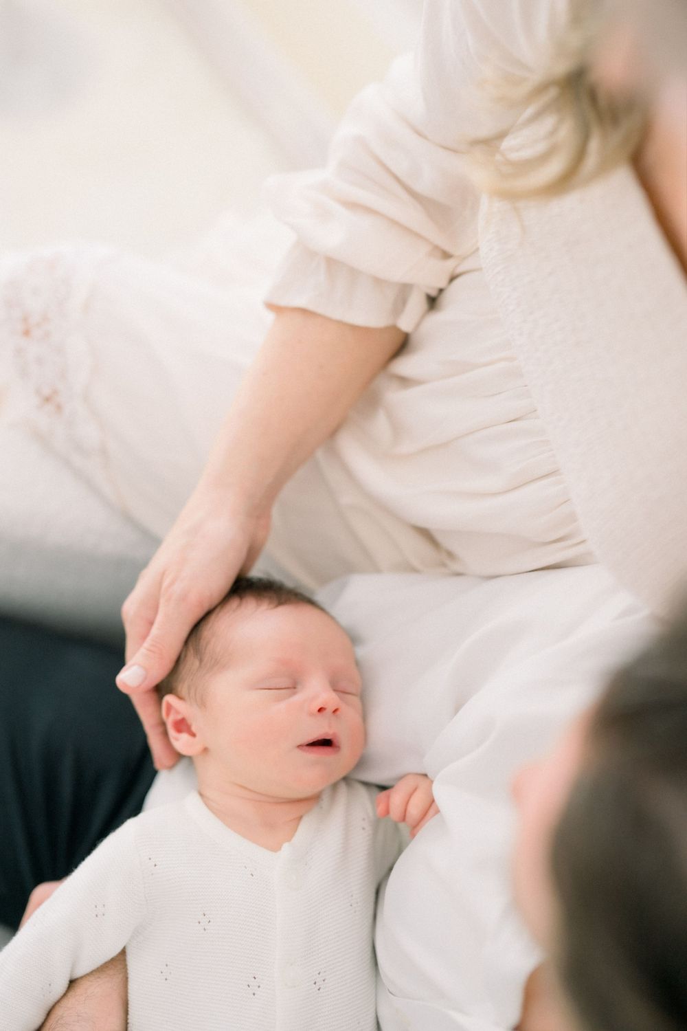 sleeping newborn baby in white clothing being cradled during an intimate portrait session taken in Northern Virginia