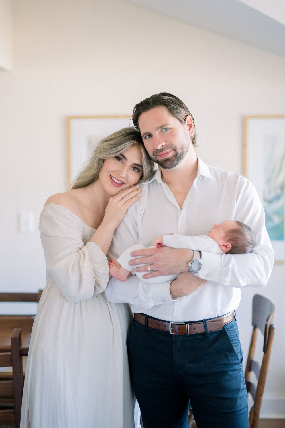 A couple embrace tenderly while holding a newborn baby in a bright indoor setting taken at a lifestyle newborn session in Washington DC