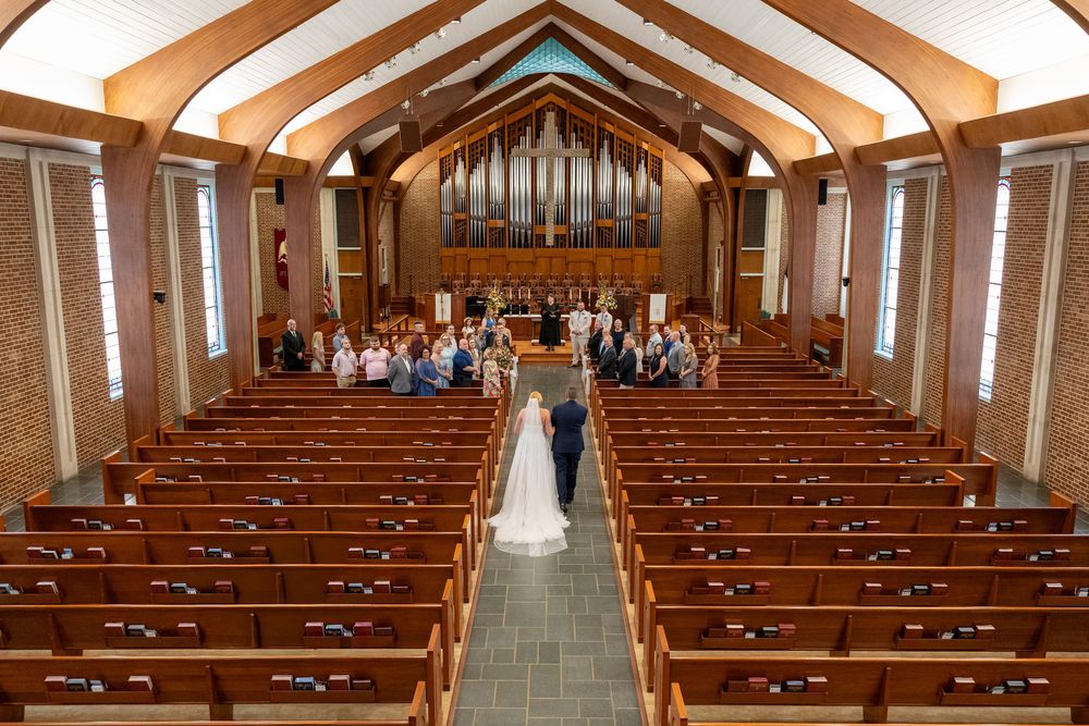 Aerial view of bride and escort walking down church aisle with wedding guests.