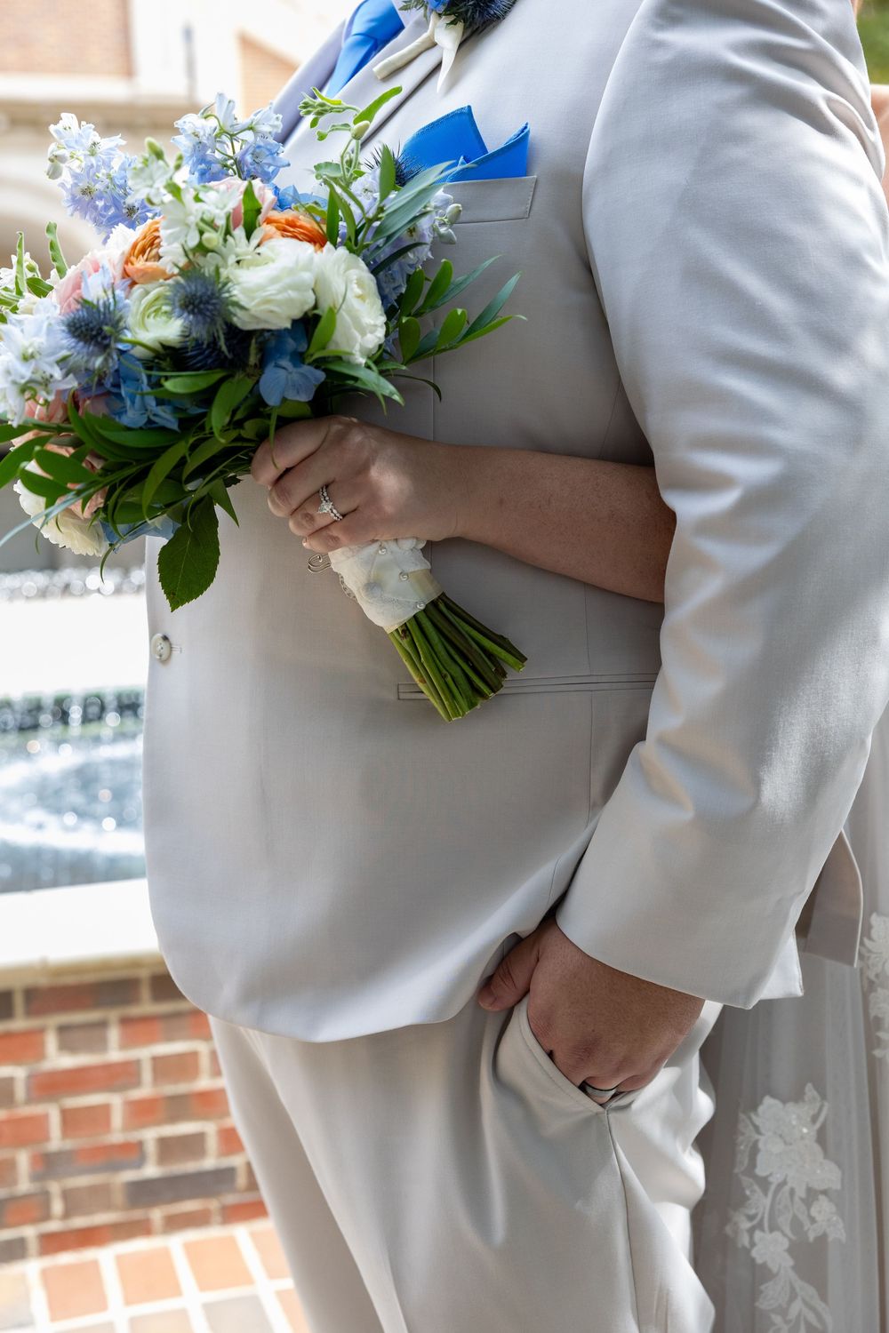 Close-up of bride and groom holding colorful blue and peach wedding bouquet.