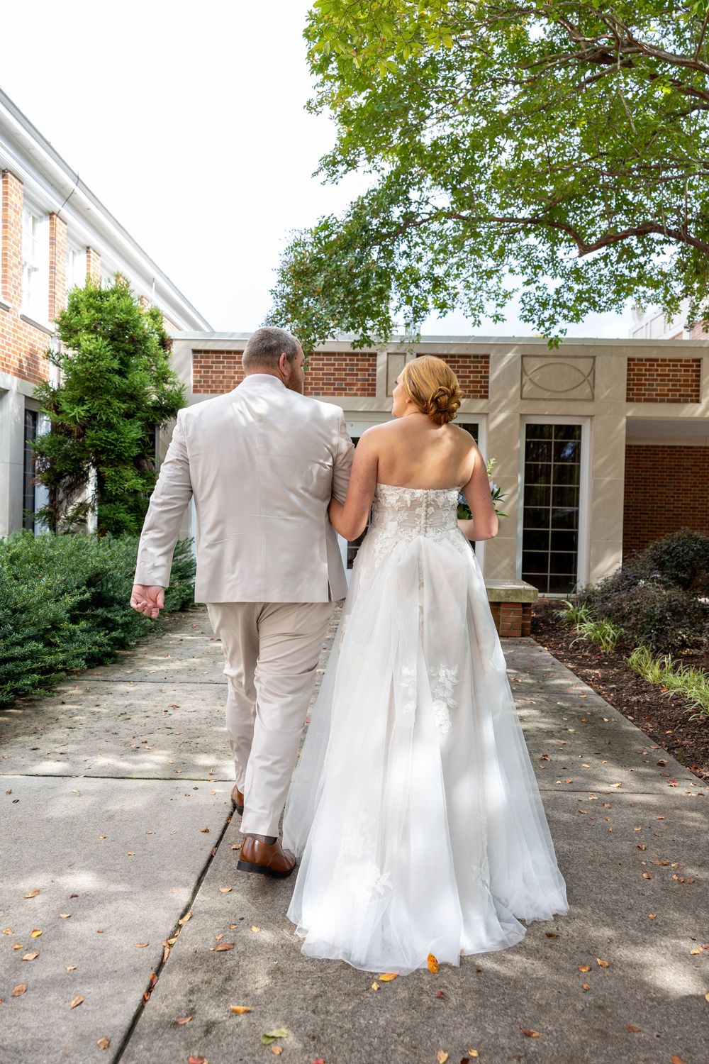 Bride and groom walking hand in hand toward brick church entrance after ceremony.