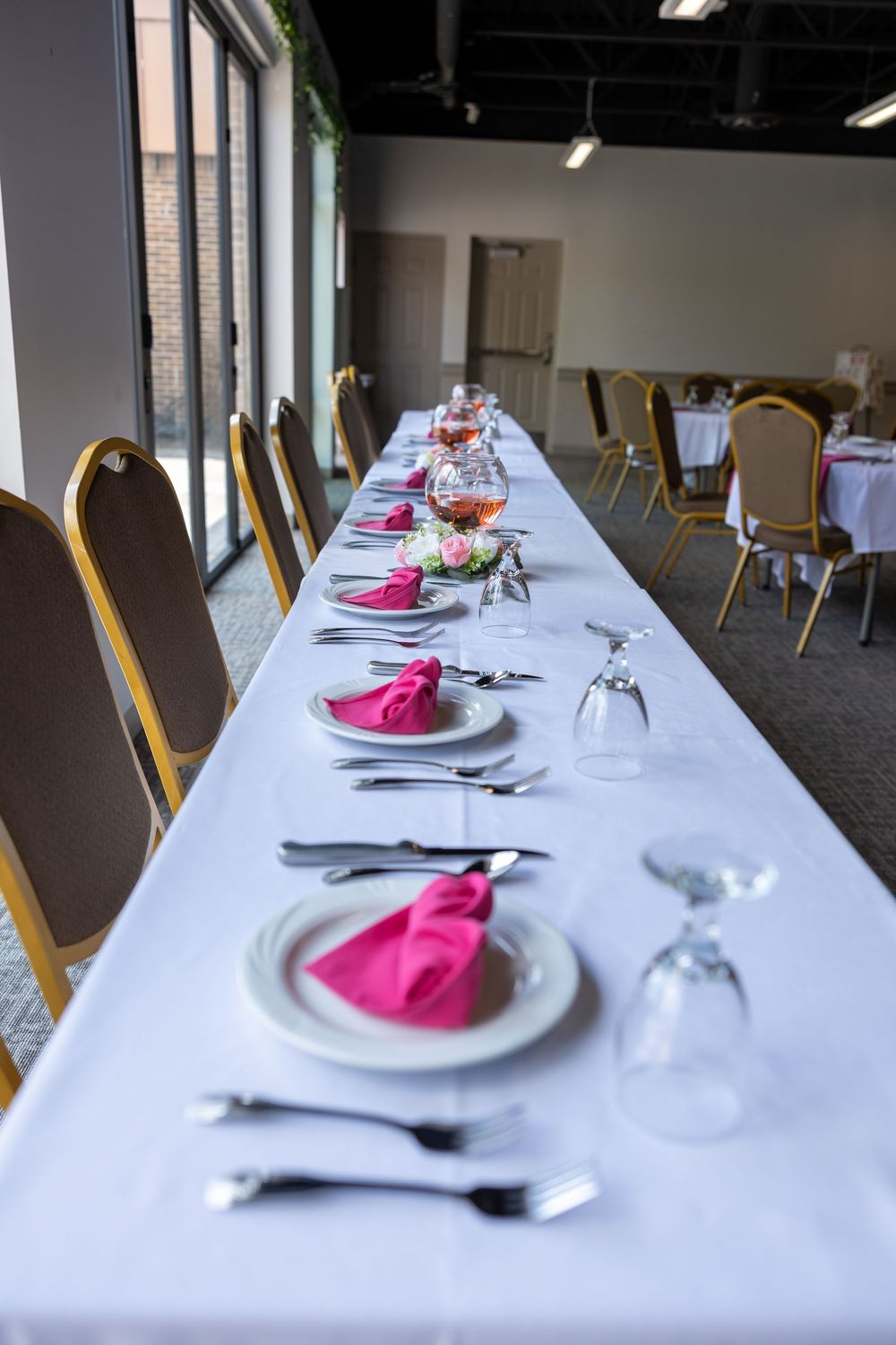 Long banquet table set with pink napkins and glassware for wedding reception dinner.