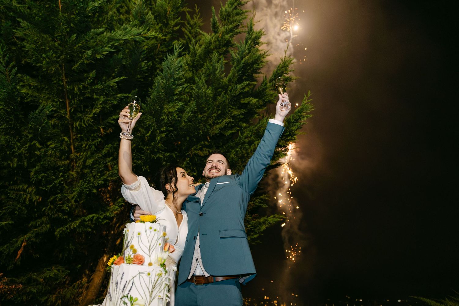 Couple celebrating their wedding during cutting cake , toasting with fireworks behind them at our quinta near Lisbon