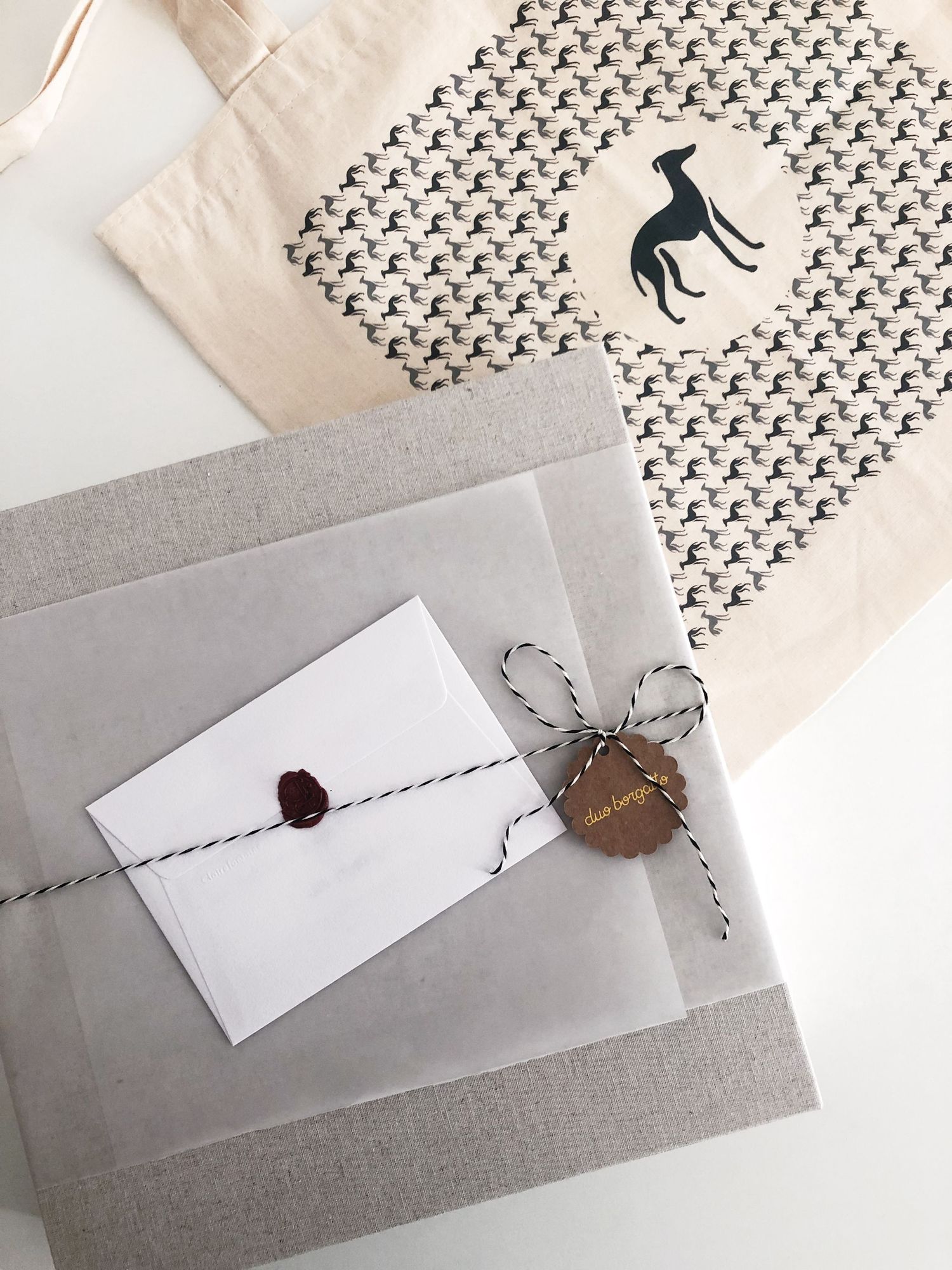 Minimalist packaging design featuring a wax-sealed envelope and tote bag with repeating dog pattern in black and white.