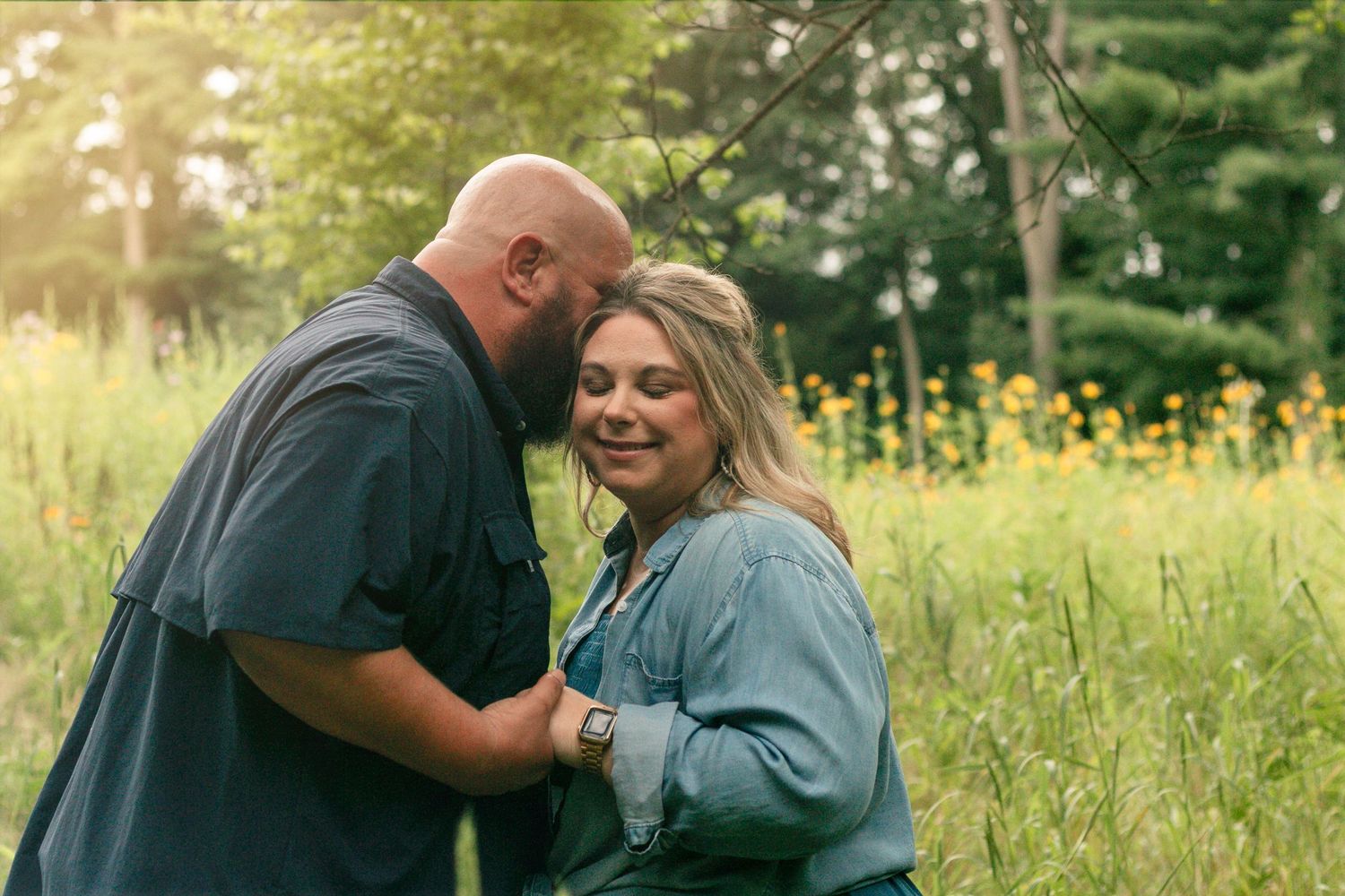 A loving couple shares an intimate moment together in a sunlit meadow with yellow wildflowers in the background.