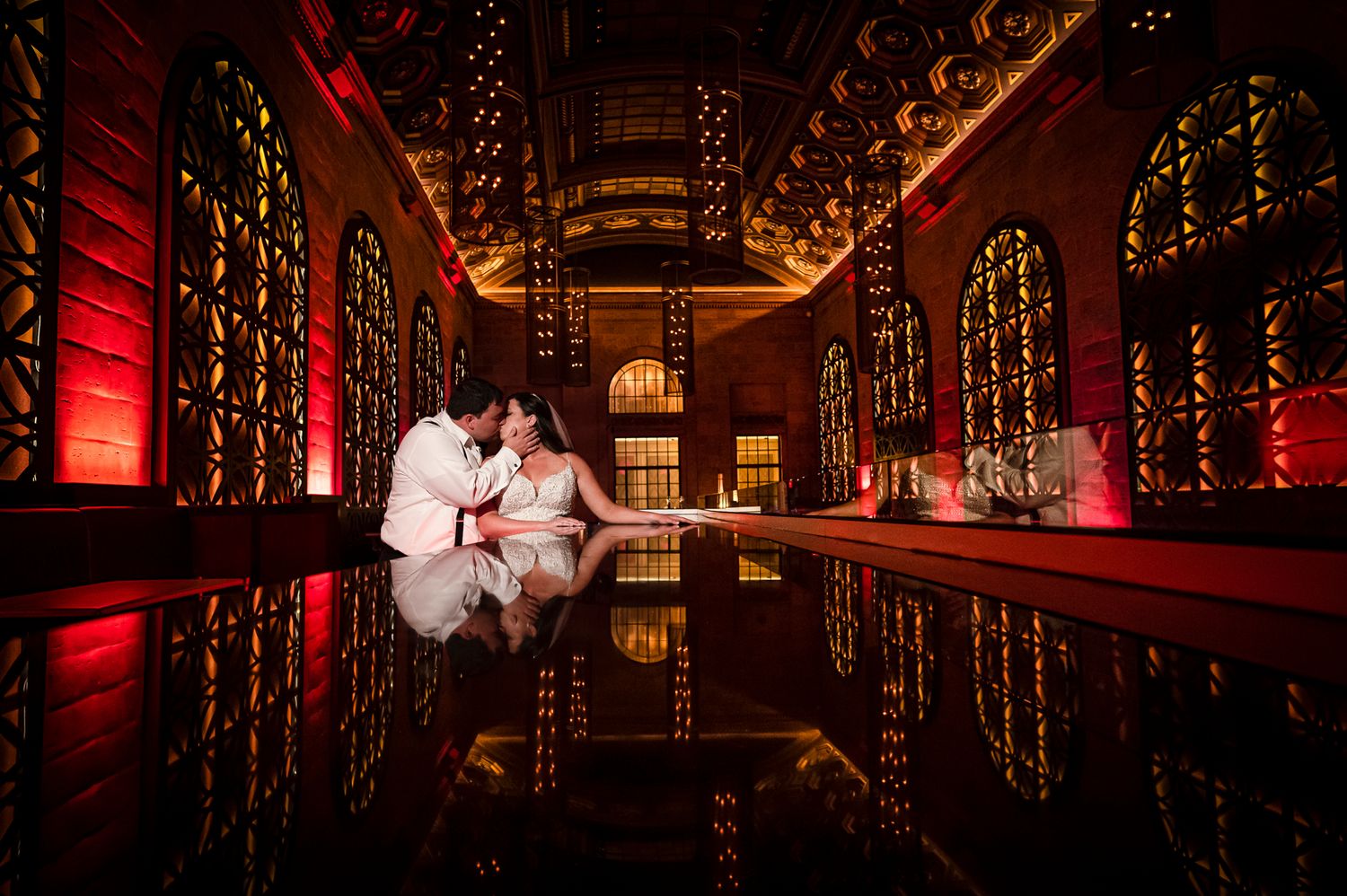 A romantic couple during their wedding at Union Trust with dramatic red lighting and reflective flooring creating a mirror effect.
