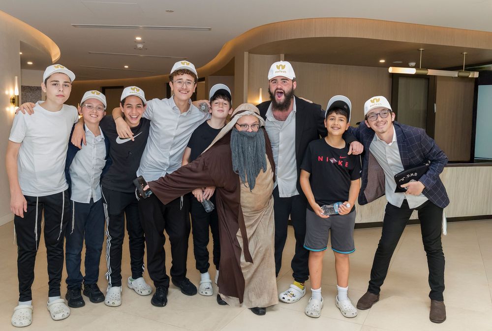 A group of people wearing white caps and casual attire pose together in an indoor hallway setting.