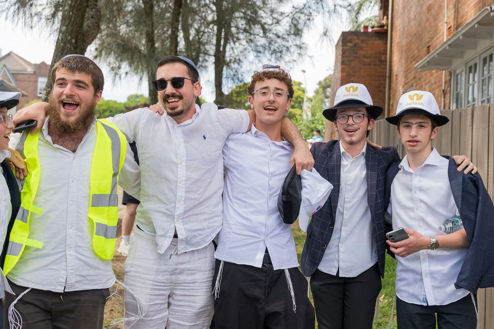 A group of people wearing white shirts and safety vests laugh and celebrate together outdoors near a brick building.