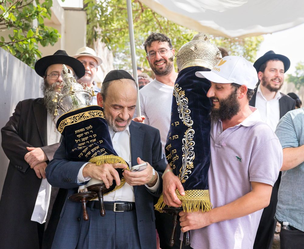 A group of Orthodox Jewish men gather outdoors under a canopy during a religious ceremony.