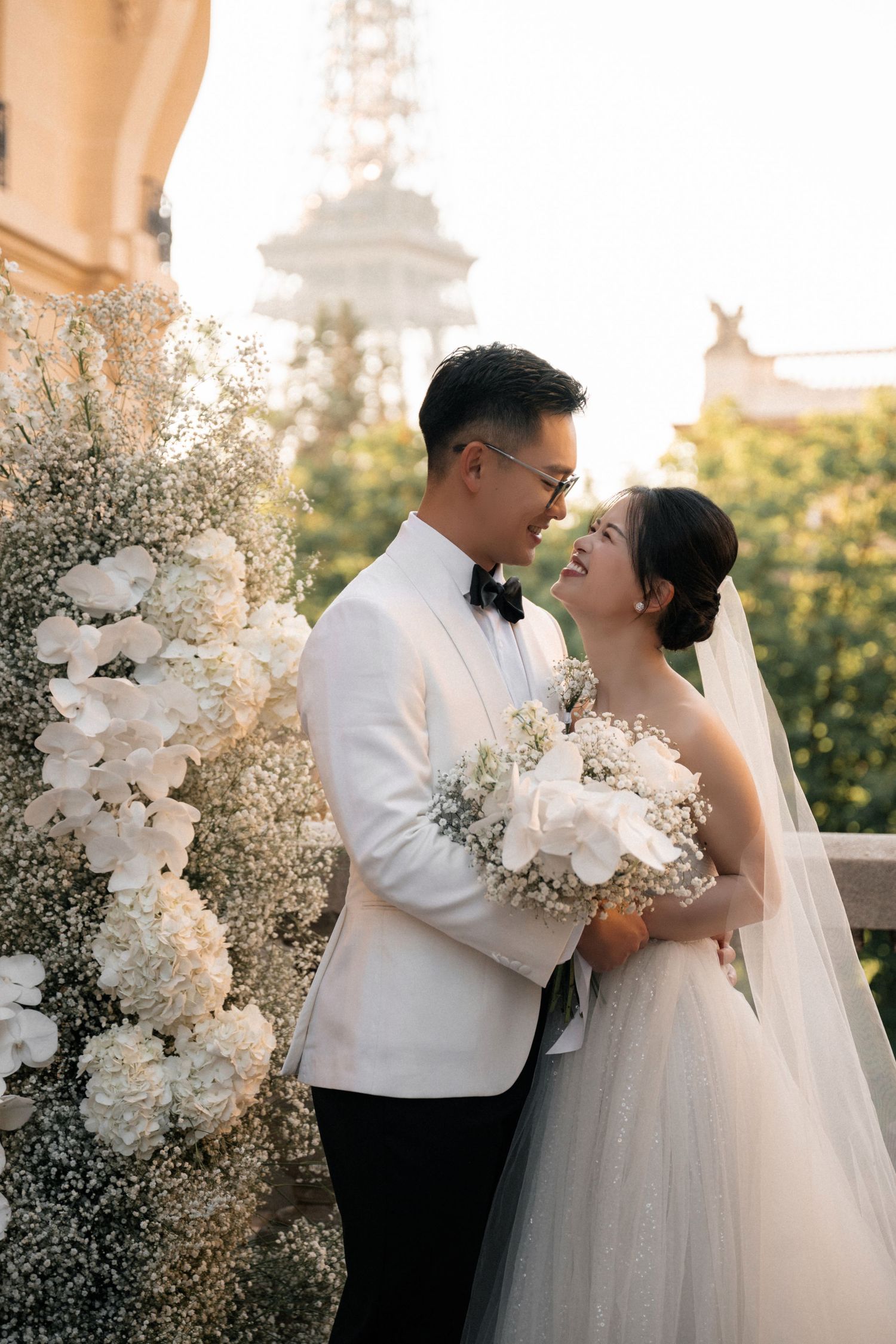 Romantic wedding couple shares intimate moments at sunset surrounded by elegant white floral arrangements and baby's breath.