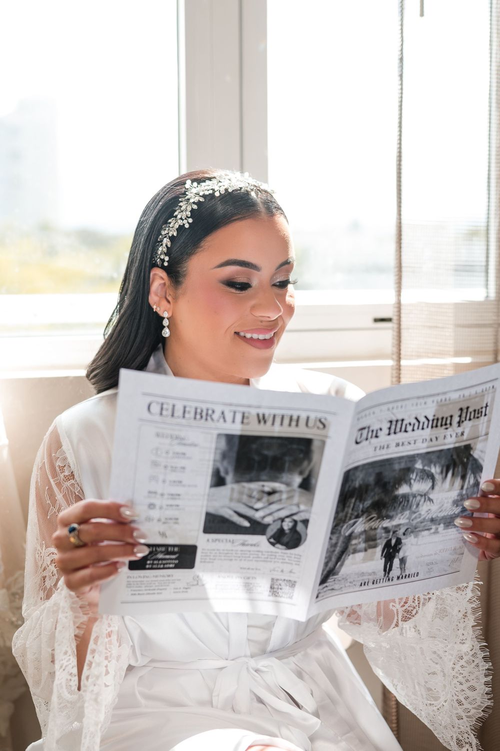 Bride in robe reading a custom newspaper by the window with soft natural light during getting ready