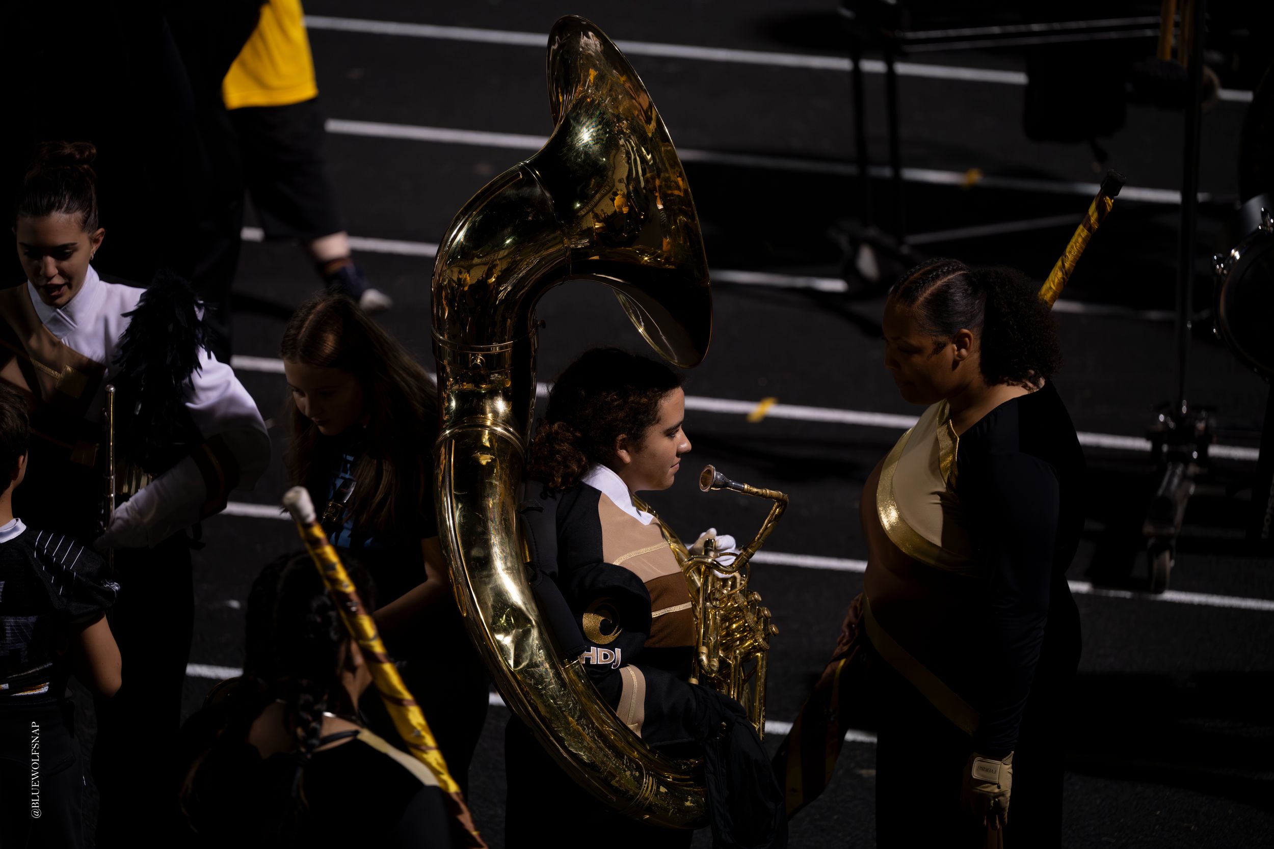 Marching band members in black uniforms playing sousaphones and brass instruments during a performance.