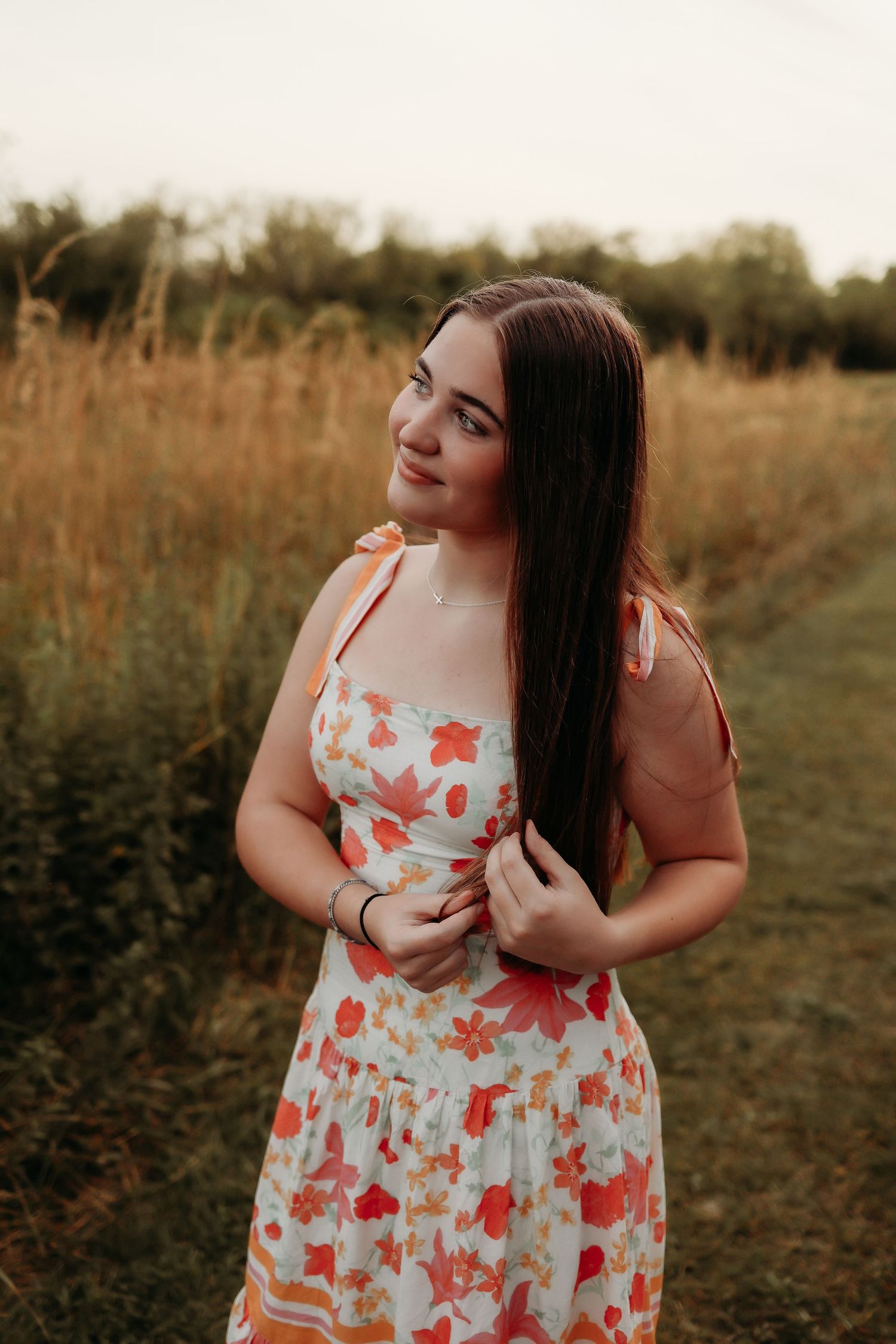Pregnant woman in white dress stands among pink flowers and sunflowers during golden hour sunset.