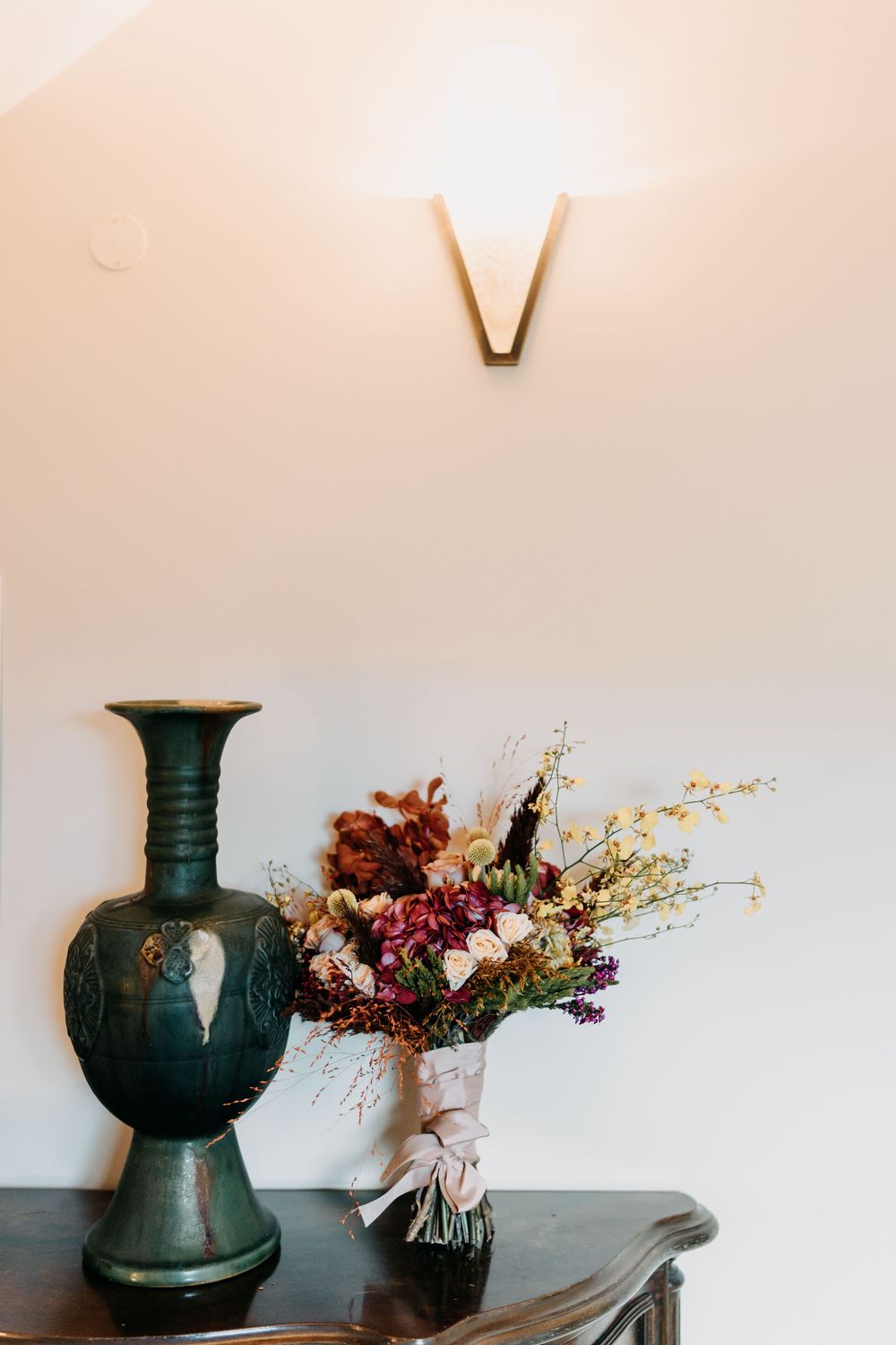 Minimalist vignette featuring dark green ceramic vases paired with dried floral arrangements on a light surface.