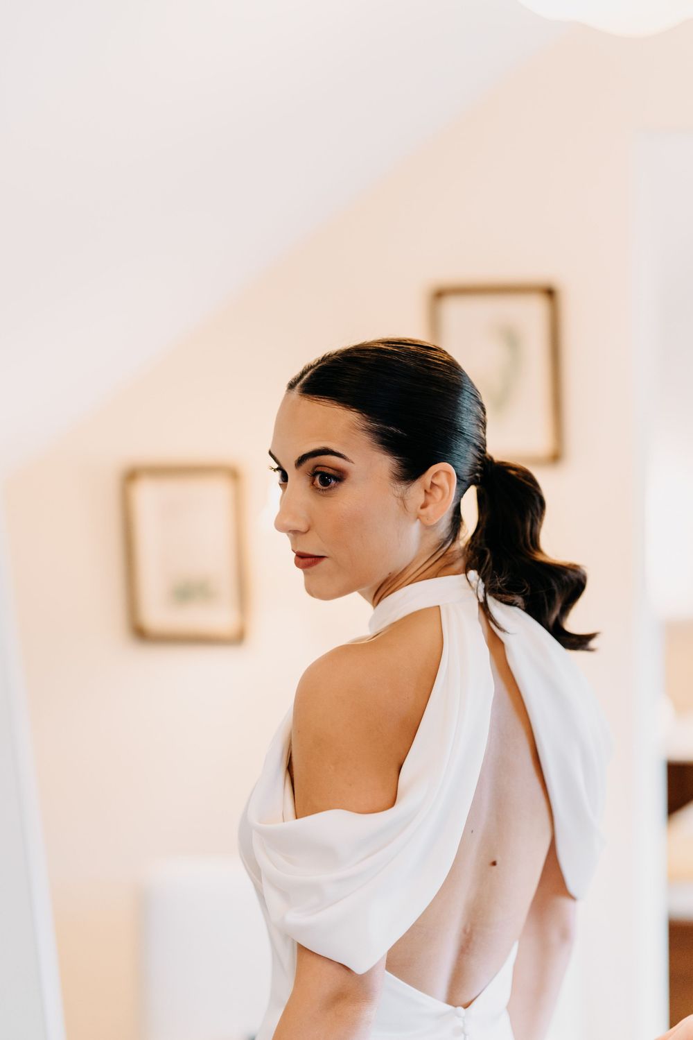 Bride in elegant white dress with dramatic draping detail shown in profile against light neutral background.