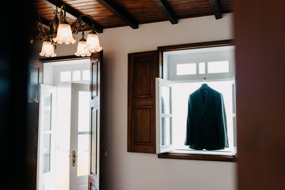 A dark suit jacket hangs in silhouette against a bright window in a rustic interior space.