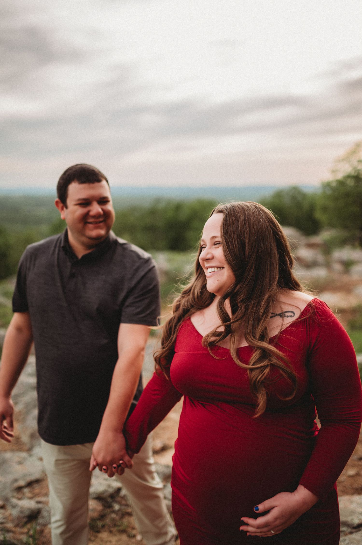 A couple in red and black attire share candid laughs during an outdoor photo session in a natural setting.